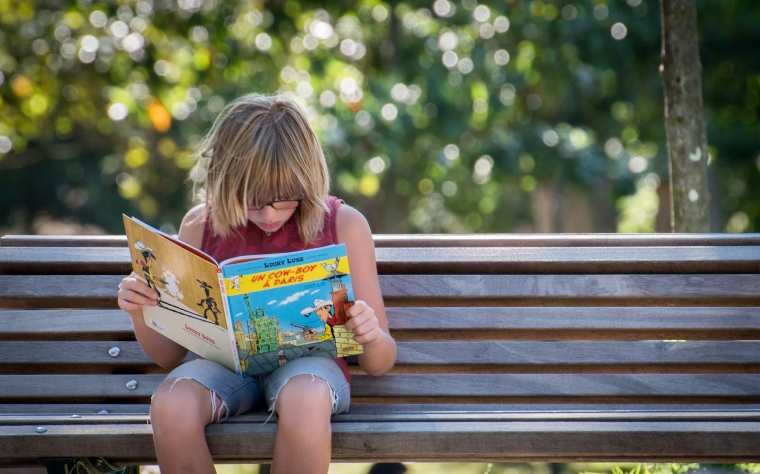 A kid reading on a bench