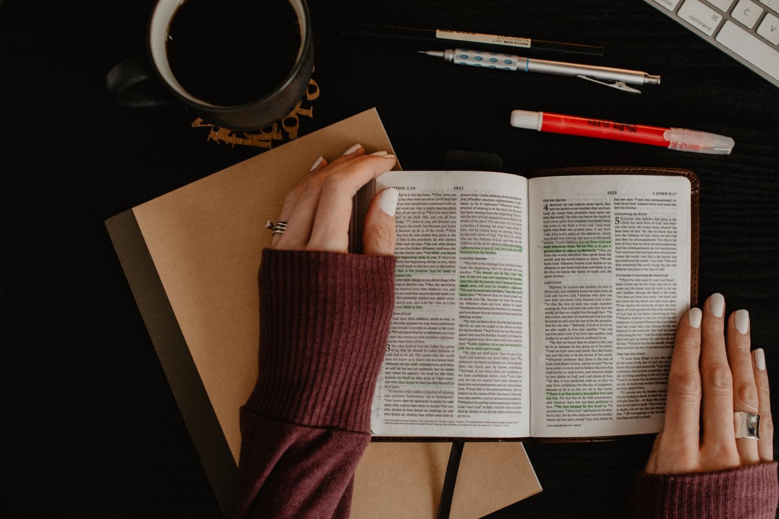An open Bible with a mug and pens on the side