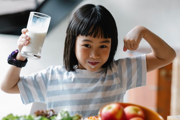 A little girl is holding up a glass of milk.